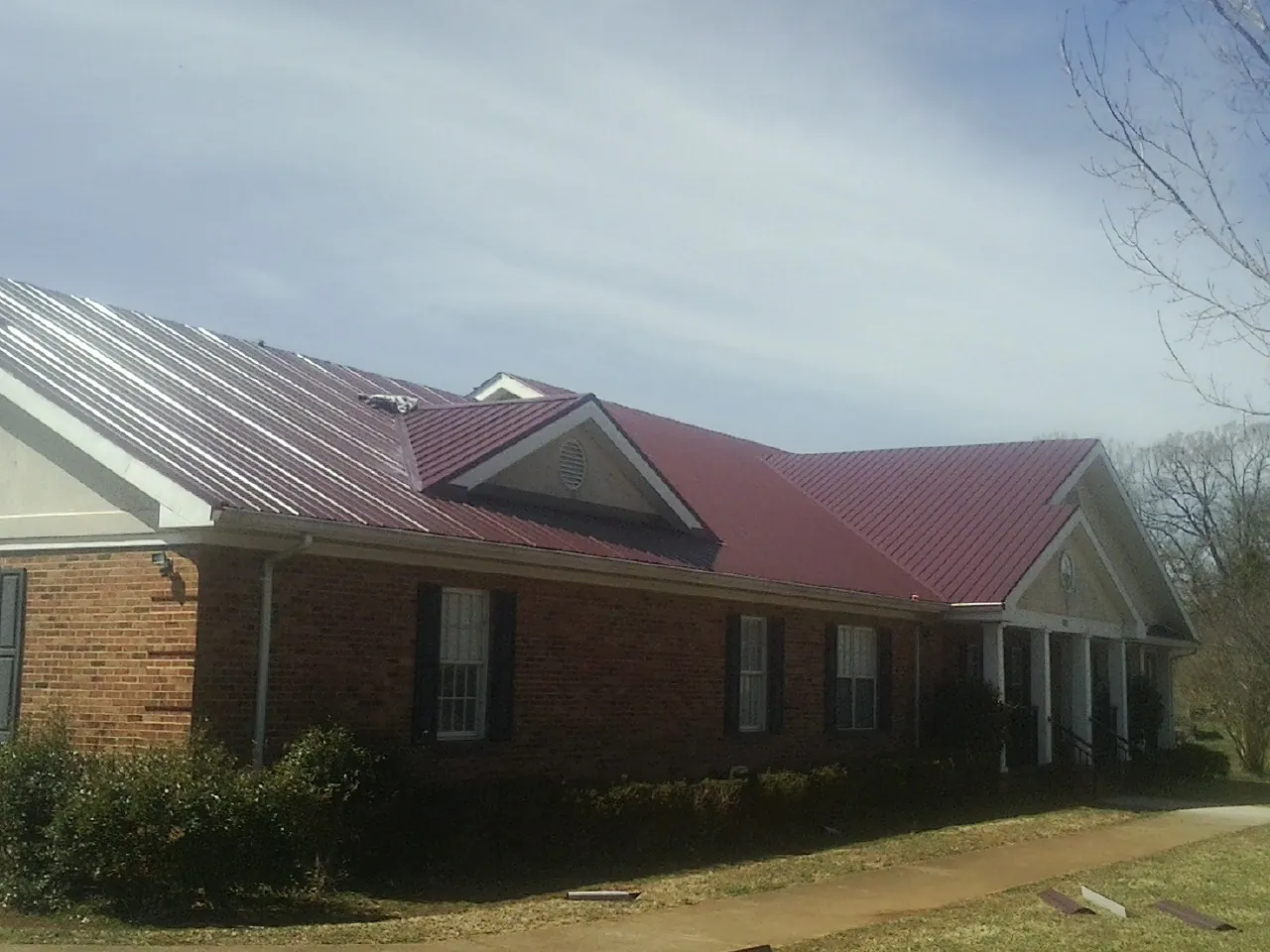 Red metal roof with gabled entries on a long brick building, from a Hail Damage Roof Repair job in Prosser